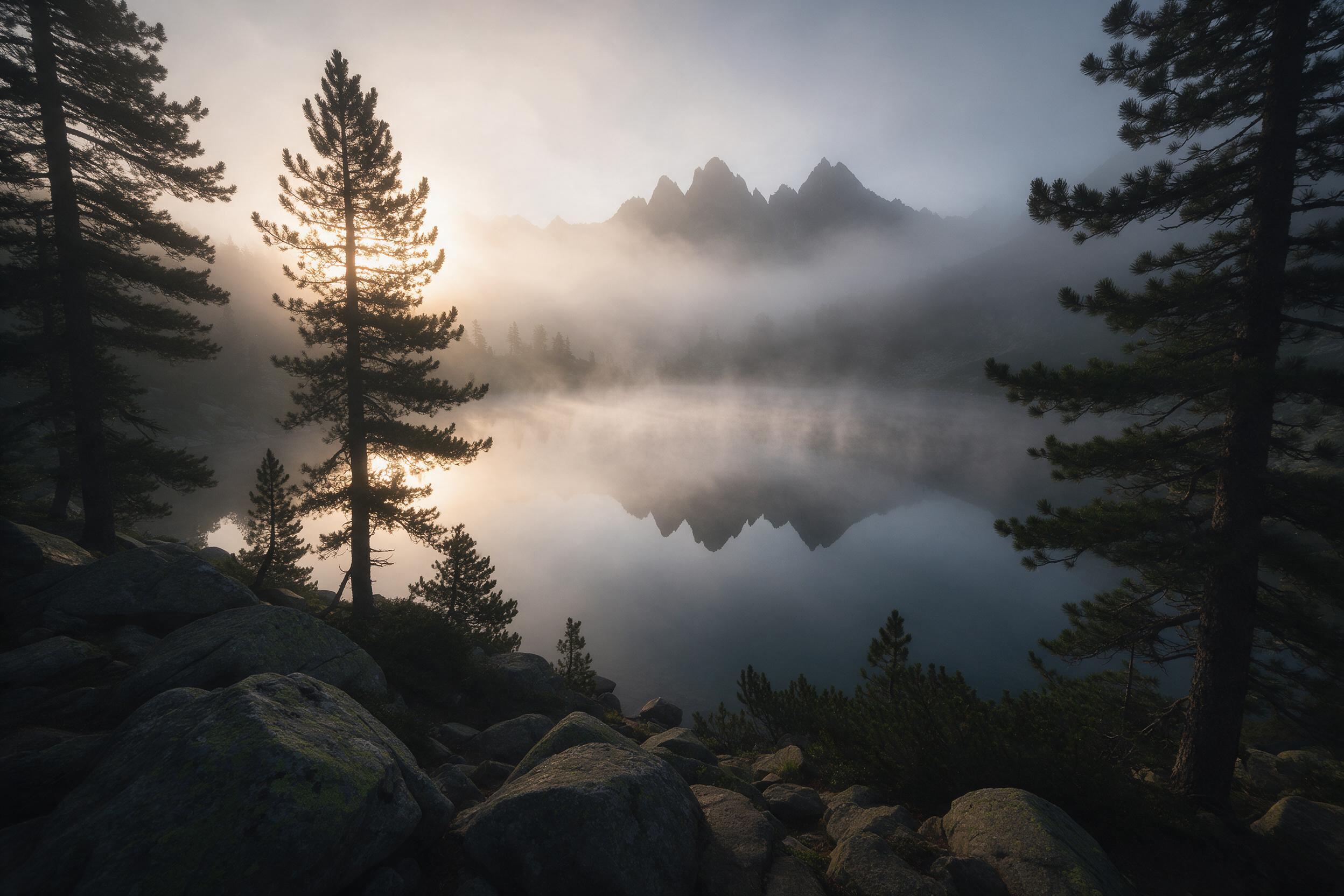 A foggy alpine lake at dawn, mirror-smooth water reflecting jagged peaks, soft golden light breaking through pine silhouettes, gentle mist drifting above surface, foreground rocks with moss detail, serene atmosphere, wide-angle composition.