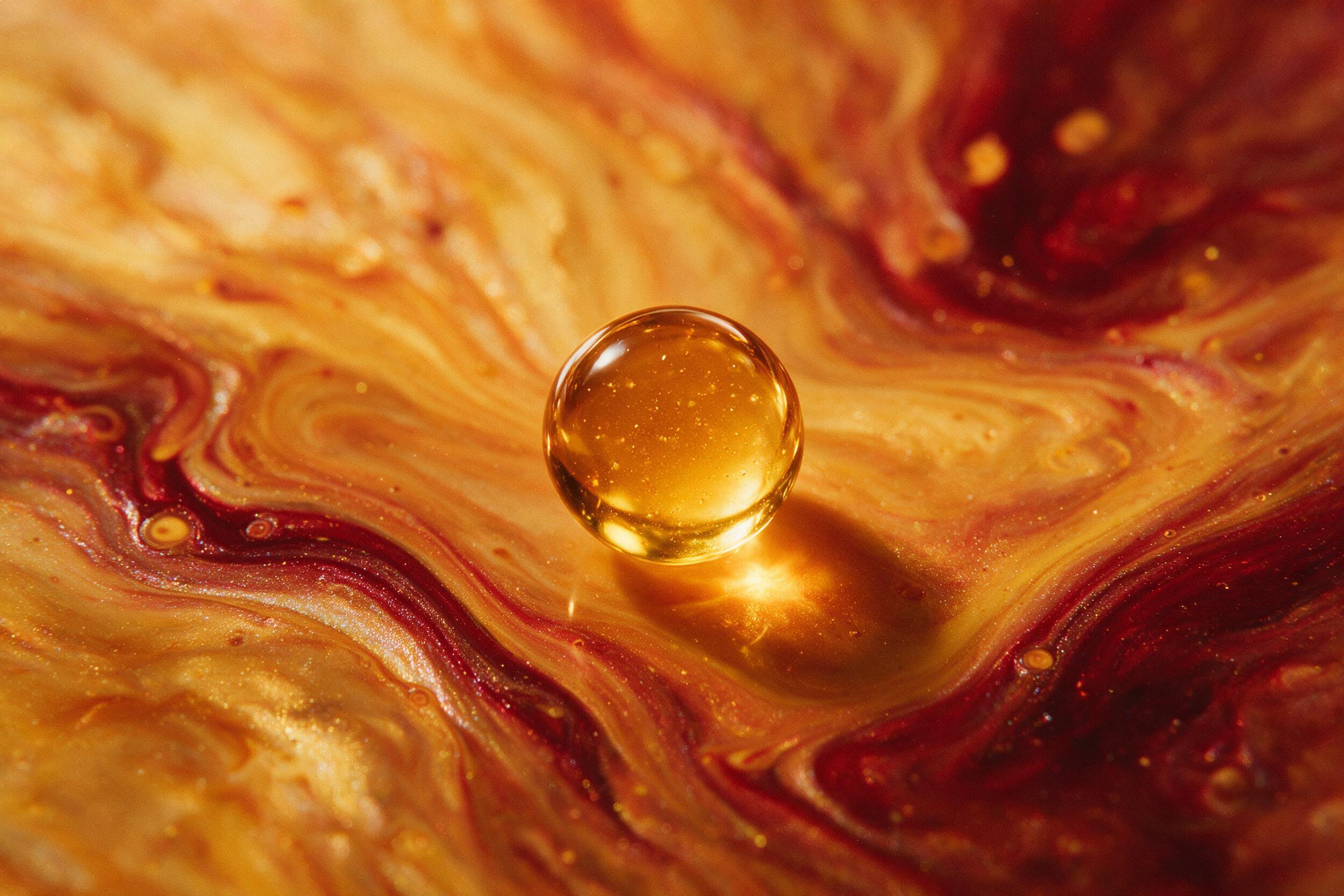 A single droplet of honey suspended mid-air, refracting golden light into a background of swirling amber and deep crimson fluid art, with soft macro focus and gentle bokeh, shot on 35mm film with slight grain