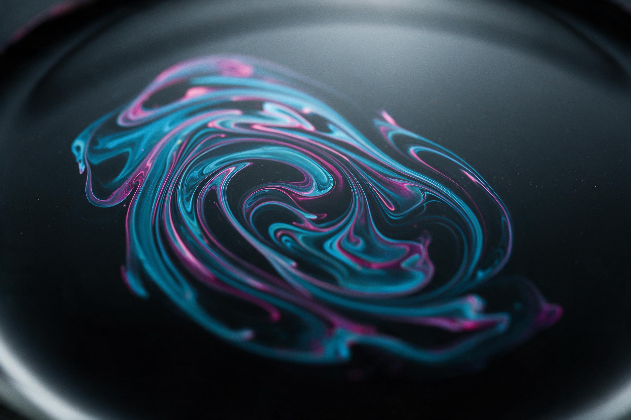 Macro shot of swirling oil and water on black glass, iridescent cyan and magenta ribbons intertwine, soft diffused lighting from above, gentle reflections, minimalist composition with negative space, subtle grain and slight blur at edges, no text or logos.