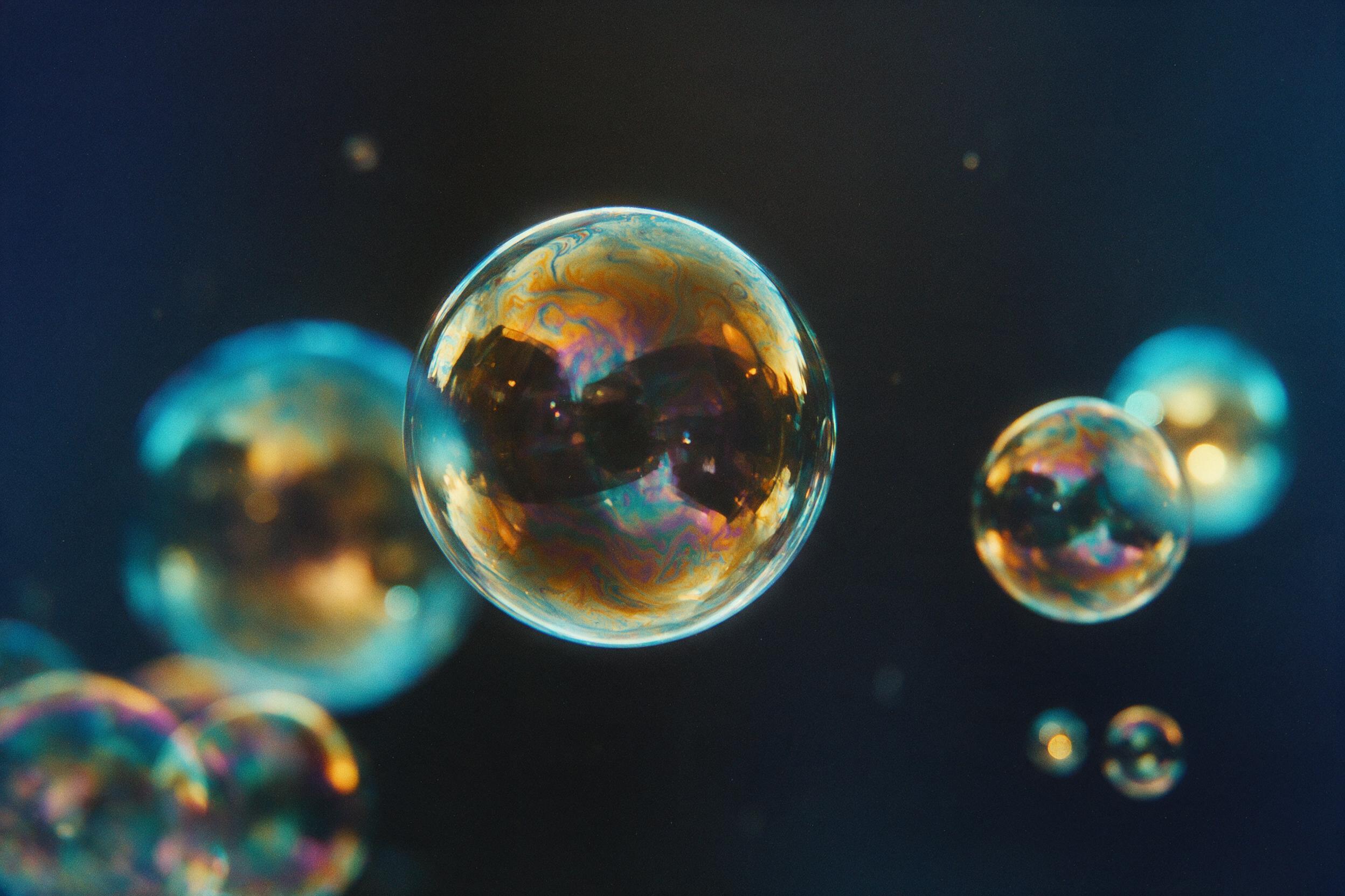 A close-up of iridescent soap bubbles floating against a dark gradient background, soft reflections, shallow depth of field, slight grain, warm amber and cool cyan lighting, minimal composition, abstract geometric shapes