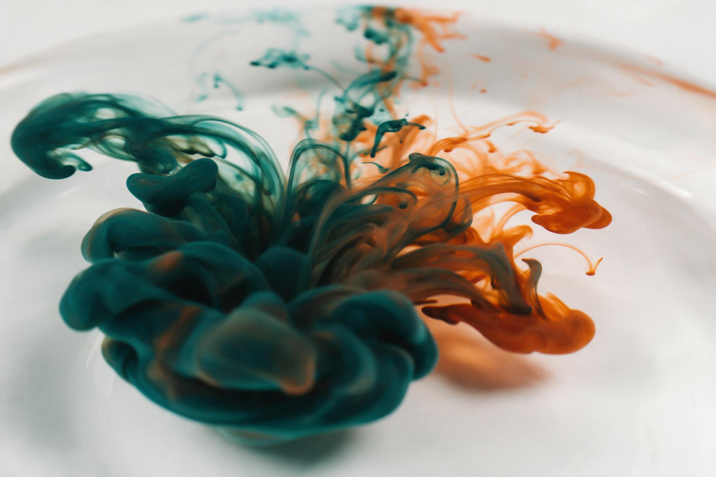 Fluid acrylic ink swirling in clear water, deep teal and burnt orange contrasting with translucent white, soft studio lighting from above, long-exposure motion blur, minimalist white background, smooth gradients and organic curves, no text or objects, clean composition with subtle reflections