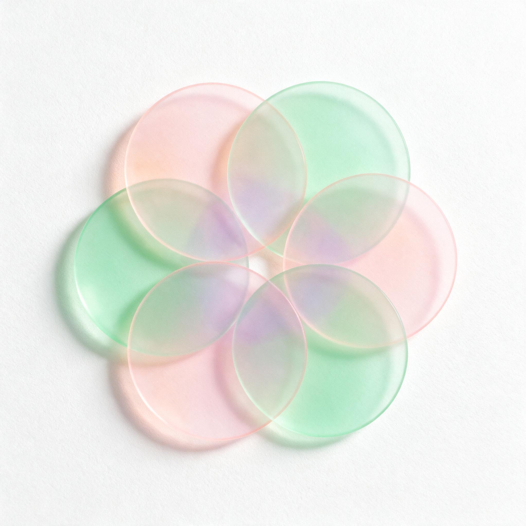 A minimalist composition of overlapping translucent pastel circles in pink and mint green, soft ambient light casting gentle shadows on a textured white surface, slight grain for a tactile feel, negative space balanced