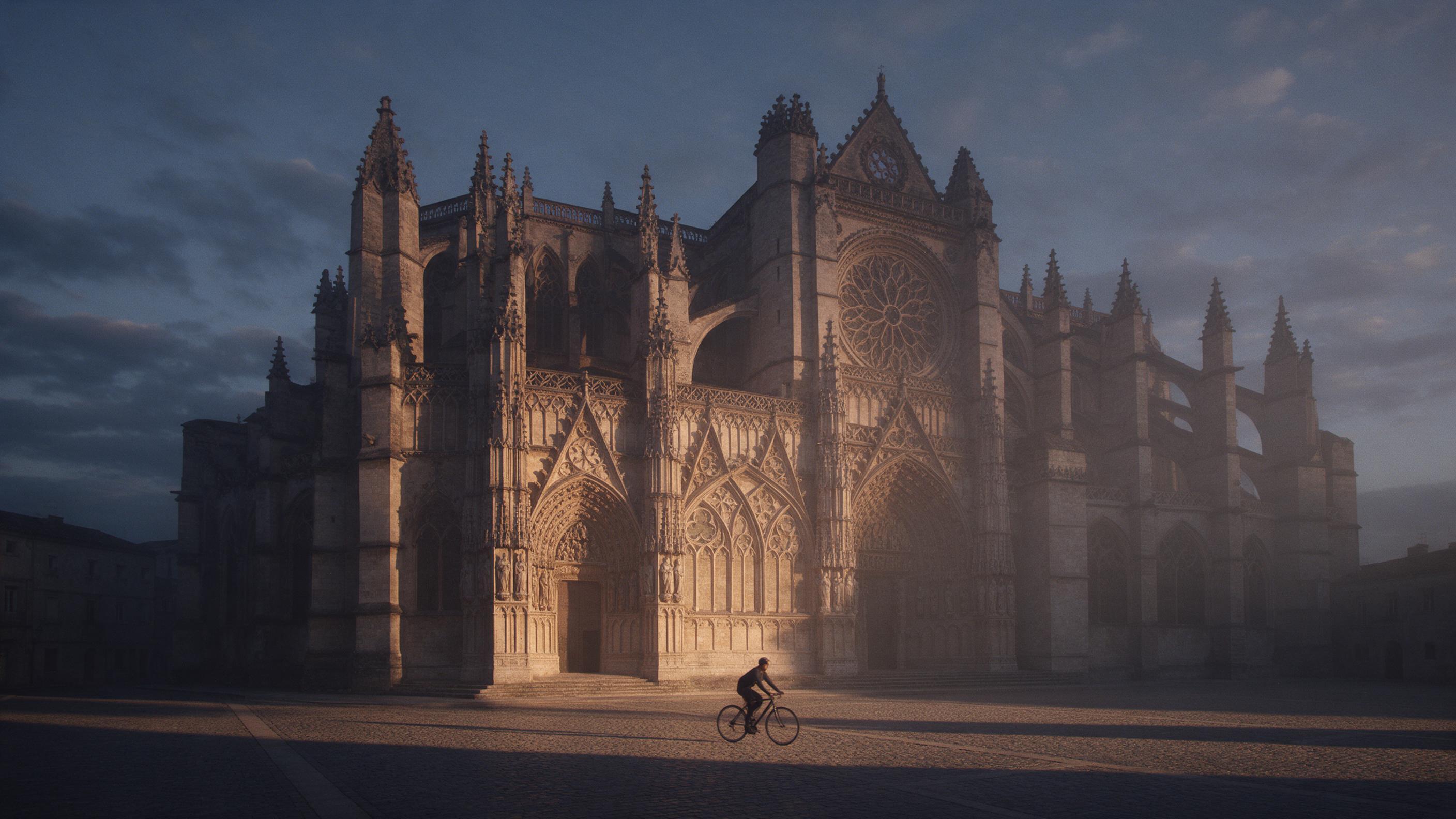 A weathered limestone cathedral facade at dawn, warm amber light raking across intricate gothic carvings, long shadows in the cobbled square, a lone cyclist passing, slight haze revealing flying buttresses and rose window, muted indigo sky with scattered clouds, film grain, natural documentary feel.