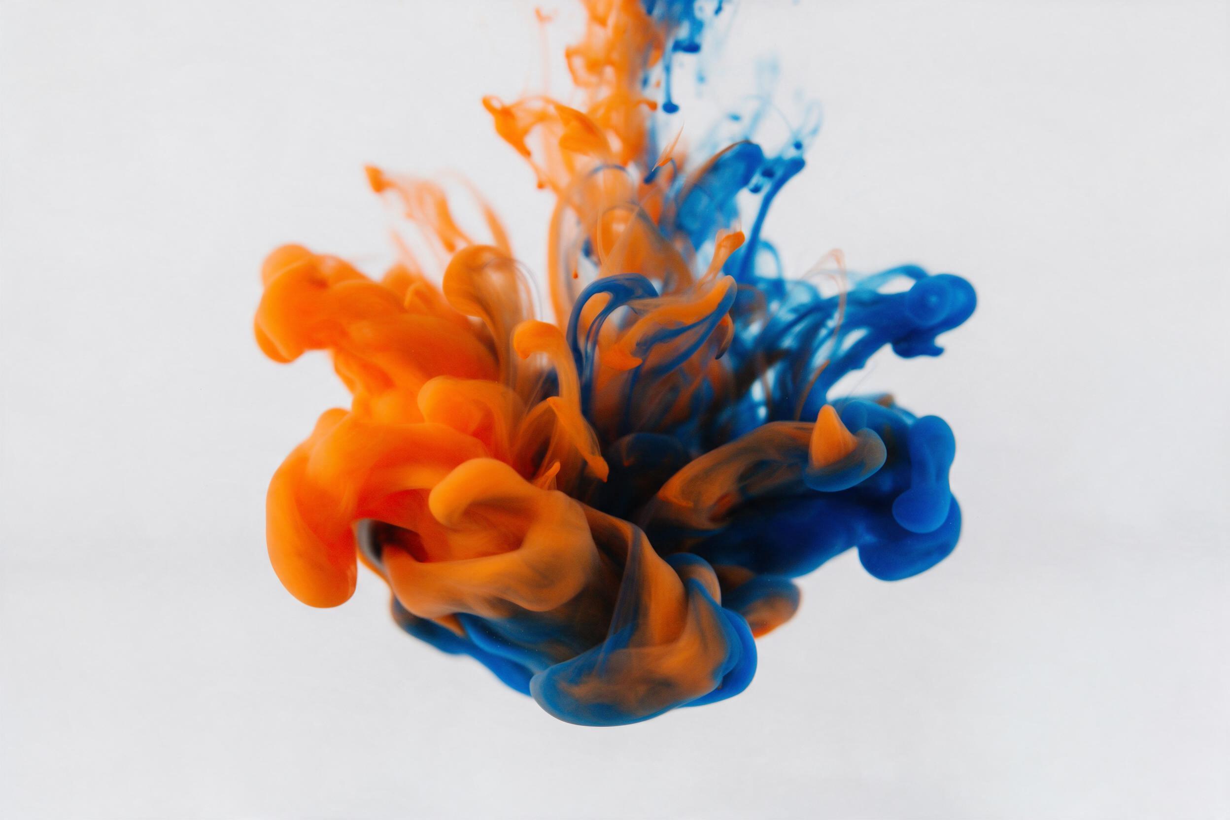 Fluid acrylic ink swirling in clear water, vibrant orange and deep blue colliding, soft studio lighting, macro shot, gentle motion blur, white background, minimalist composition with negative space.